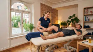 Physiotherapeutin behandelt das Bein eines Patienten in einer gemütlichen Praxis, Symbolbild zu Heilbehandlungskosten nach einem Unfall